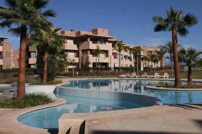 a swimming pool with palm trees in front of a building at golf city Av Med VI in Marrakech