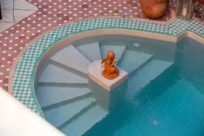 a statue of a woman sitting on a bench next to a swimming pool at Indian Palace in Marrakech