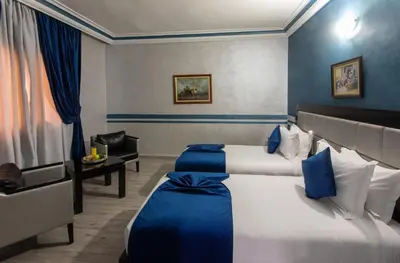 a hotel room with two beds and a chair at Hotel Meriem Marrakech in Marrakech
