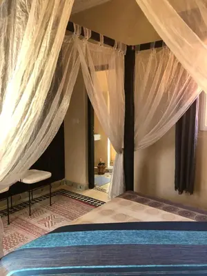 a bedroom with a bed with curtains and a chair at Riad Côté palmeraie in Marrakech