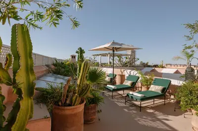 a patio with chairs and an umbrella and plants at Dar Lalla F'dila in Marrakech