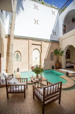 a courtyard with a swimming pool with two benches at Riad Amira in Marrakech