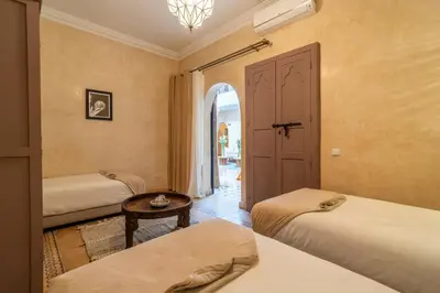 a bedroom with two beds and a table and a door at Riad Beldi in Marrakech