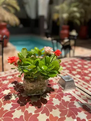 a vase with flowers on a table with a pool at Riad Pachavana in Marrakech