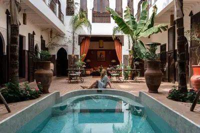 a woman sitting next to a swimming pool in a courtyard at Riad Pachavana in Marrakech