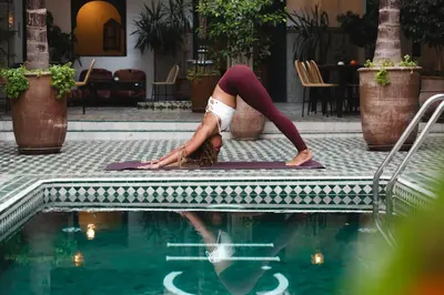 a woman doing a yoga pose next to a swimming pool at The Central House Marrakech Medina in Marrakech