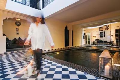 a woman walking on a checkered floor next to a swimming pool at Riad Elizabeth in Marrakech