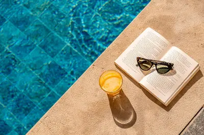 a book and glasses on a table next to a swimming pool at Grand Plaza Marrakech in Marrakech