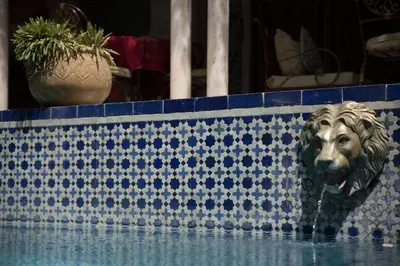 a lion head on the side of a blue and white tile pool at Riad Palais Sebban in Marrakech