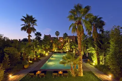 a swimming pool with chairs and palm trees at night at Tigmiza Boutique Hotel & Spa in Marrakech