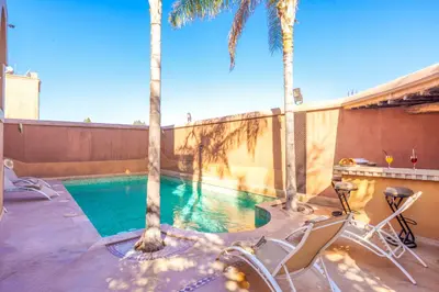 a swimming pool with palm trees and chairs on a patio at Riad Ushuaia - Centre Marrakech in Marrakech