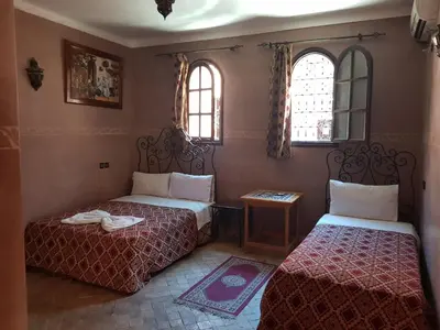 two beds in a room with two windows at Hotel Wissam in Marrakech