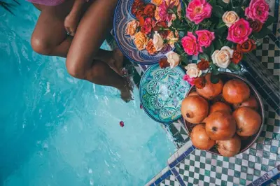 a table with a bowl of fruit and flowers next to a pool at Riad Tamarrakecht in Marrakech