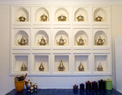 a white wall with a shelf filled with gold teapots at Riad Le J in Marrakech