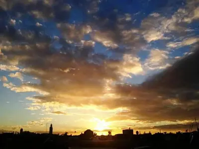 a cloudy sky with the sun setting in the city at Riad Alkaderi in Marrakech