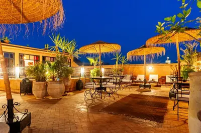 a patio with tables and chairs and umbrellas at night at Riad Dar Nadwa in Marrakech