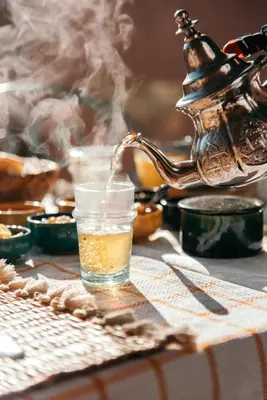 a glass of tea is sitting on a table with a tea kettle at Riad Albatoul in Marrakech