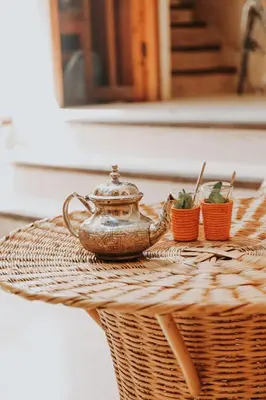 a tea pot on a wicker table with two plants at Dar Nour el Houda in Marrakech