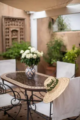 a straw hat sitting on a table with a vase of flowers at Riad Mur Akush in Marrakech