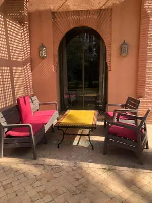 a patio with two chairs and a table with pink cushions at la palmeraie village Appartement in Marrakech