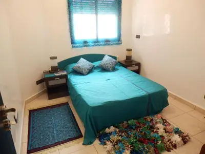 a bedroom with a bed with a green comforter and a window at Appart Piscine Jardin somptueux à 2 min de palmeraie et 10 min de Majorelle in Marrakech