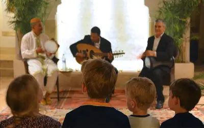 a group of children listening to a man playing guitar at Riad Dar Housnia in Marrakech