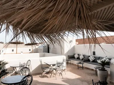 a patio with tables and chairs under a straw roof at Riad Louhou in Marrakech