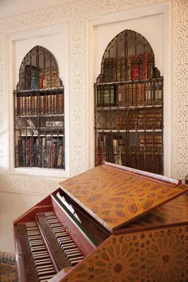 a piano in a room with shelves of books at Riad Ifoulki in Marrakech