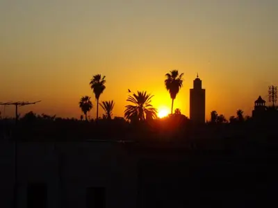 a sunset with palm trees and a clock tower at Riad Al Ksar & Spa in Marrakech