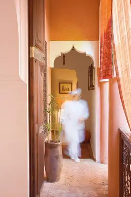 a man walking down a hallway with a plant at Dar Attajmil in Marrakech