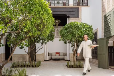 a man holding a plate in a courtyard with trees at Le Farnatchi in Marrakech