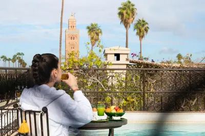 a woman sitting at a table taking a picture of a clock tower at La Villa des Orangers - Relais & Châteaux in Marrakech