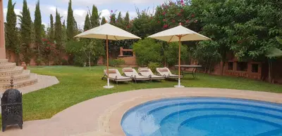 a swimming pool with two umbrellas and chairs and a table at Villa clos Odette in Marrakech