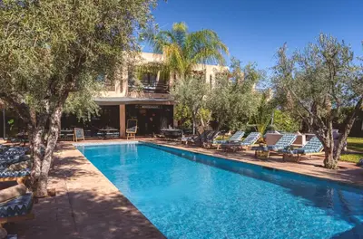 a swimming pool with chairs and trees and a building at Boutique Hotel Katia in El Harkat