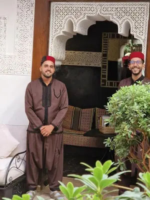 two men wearing red turbans standing in front of a bed at Riad Les Nuits de Marrakech in Marrakech