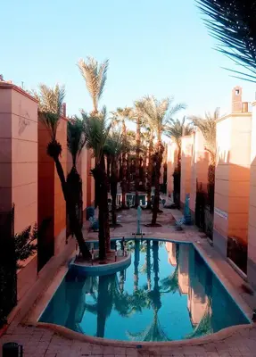 a swimming pool with palm trees in a courtyard at Riad Ansar in Marrakech