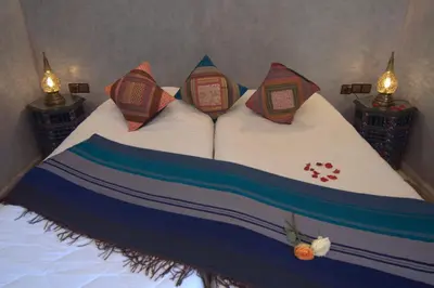 a bed with three pillows on it with two lamps at Riad Imilchil in Marrakech