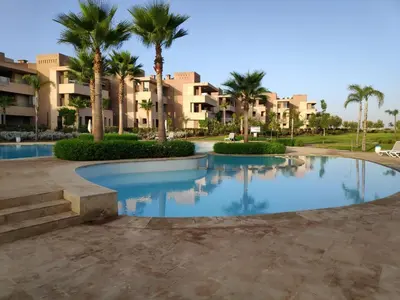 a swimming pool in a resort with palm trees and buildings at Magnifique appart vue sur golf in Marrakech