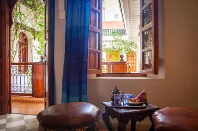 a table and two stools in a room with windows at Riad Sable Chaud in Marrakech
