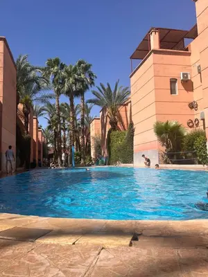 a large blue swimming pool with palm trees and buildings at Riad Hicham in Marrakech in Marrakech