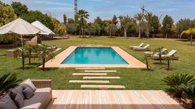 a swimming pool in the middle of a grassy yard with chairs at Mimouna Riads in Marrakech