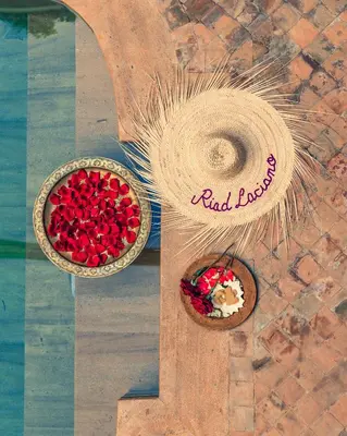 two bowls of red flowers and a hat on a table at Riad Luciano Hotel and Spa in Marrakech