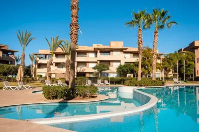 a swimming pool with palm trees in front of a building at Coup de cœur à Marrakech - idéal famille et couple in Marrakech