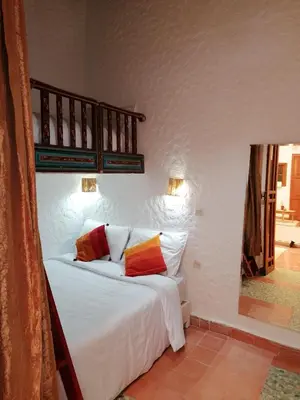 a bedroom with a bed with white sheets and colorful pillows at DAR MAR'OUKA , Maison d'hôtes in Marrakech