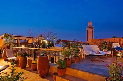 a rooftop patio with chairs and a clock tower at Riad Cinnamon by Marrakech Riad in Marrakech