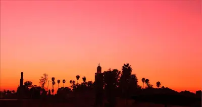 a sunset with palm trees and a clock tower at Riad Hôtel Marraplace in Marrakech