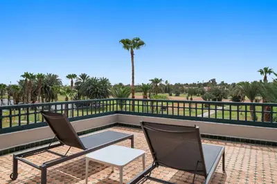 two chairs and a table on a balcony with palm trees at Palmeraie Golf Suites By Pickalbatros in Marrakech