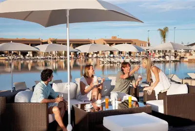 a group of people sitting under an umbrella by a pool at Hotel Riu Tikida Palmeraie - All Inclusive in Marrakech
