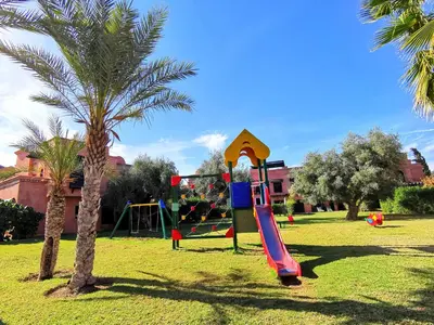 a playground with a slide in a park with a palm tree at La Perle de l'Atlas by Golf Resort in Marrakech