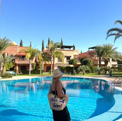 a woman in a hat standing in front of a swimming pool at La Perle de l'Atlas by Golf Resort in Marrakech